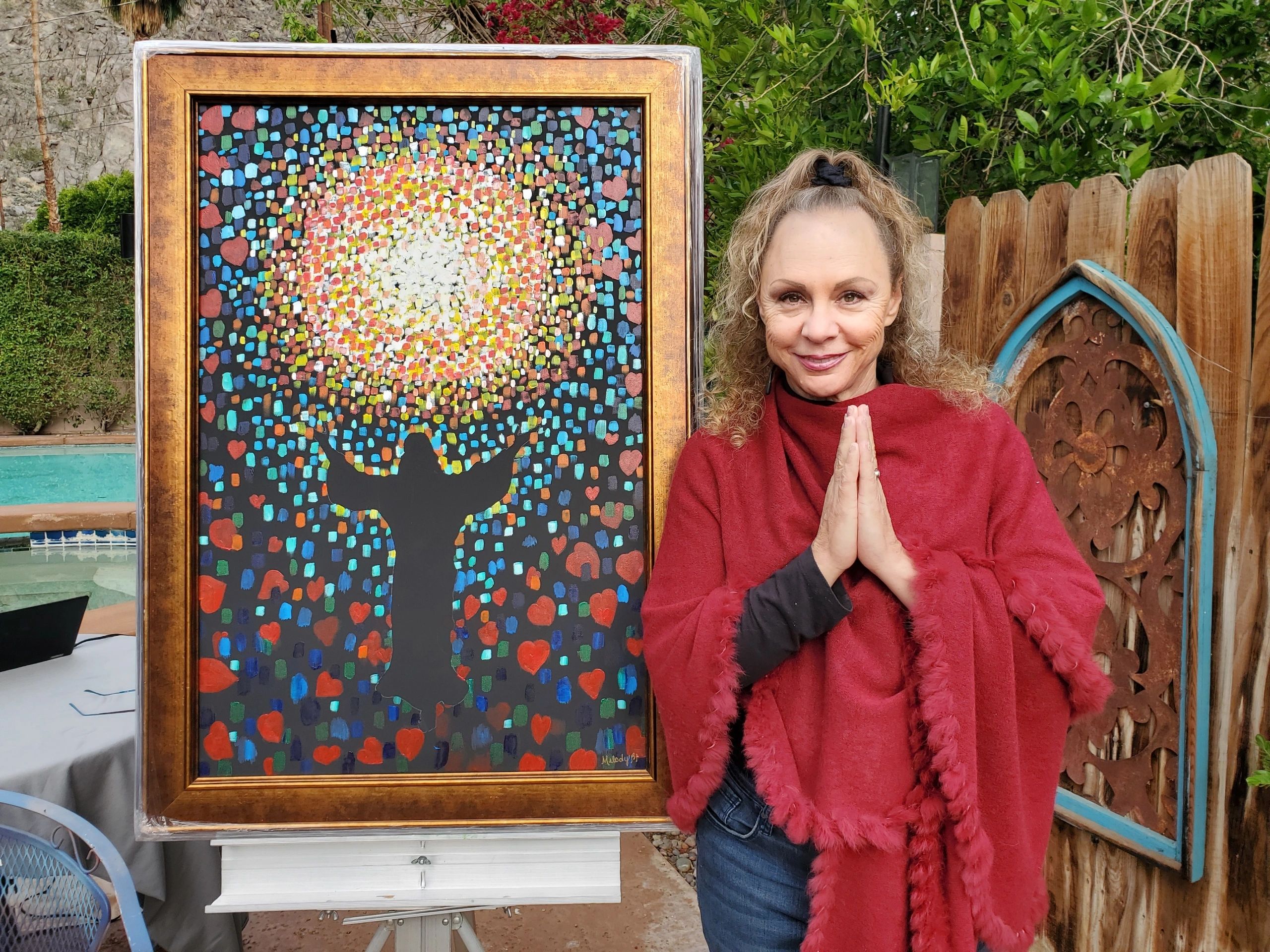 Melody standing next to her colorful mosaic artwork in the garden